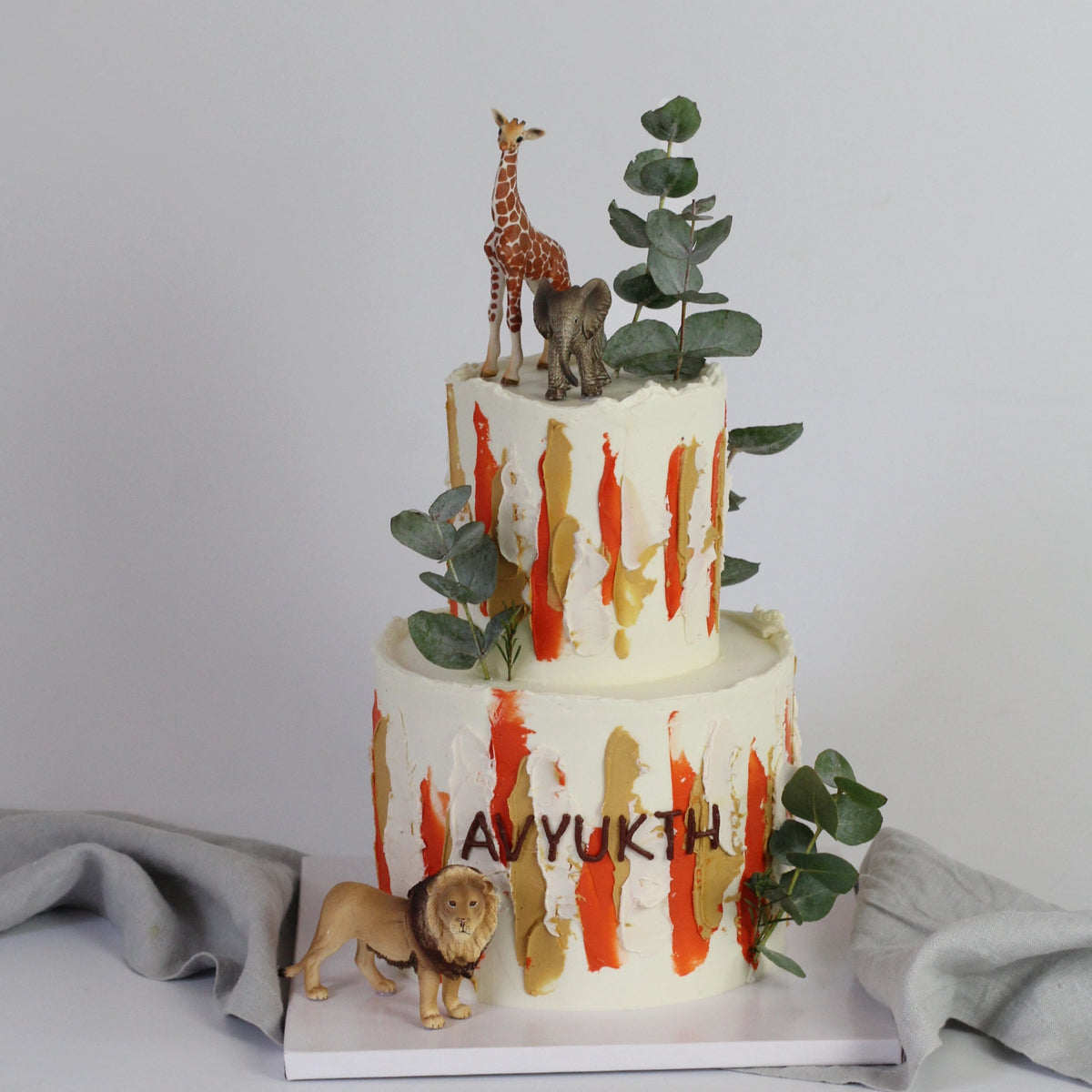 Der Safari Tour Cake – perfekt für alle, die weg wollen! Geschmückt mit Pinselstrichen, Blättern und einer Figur.