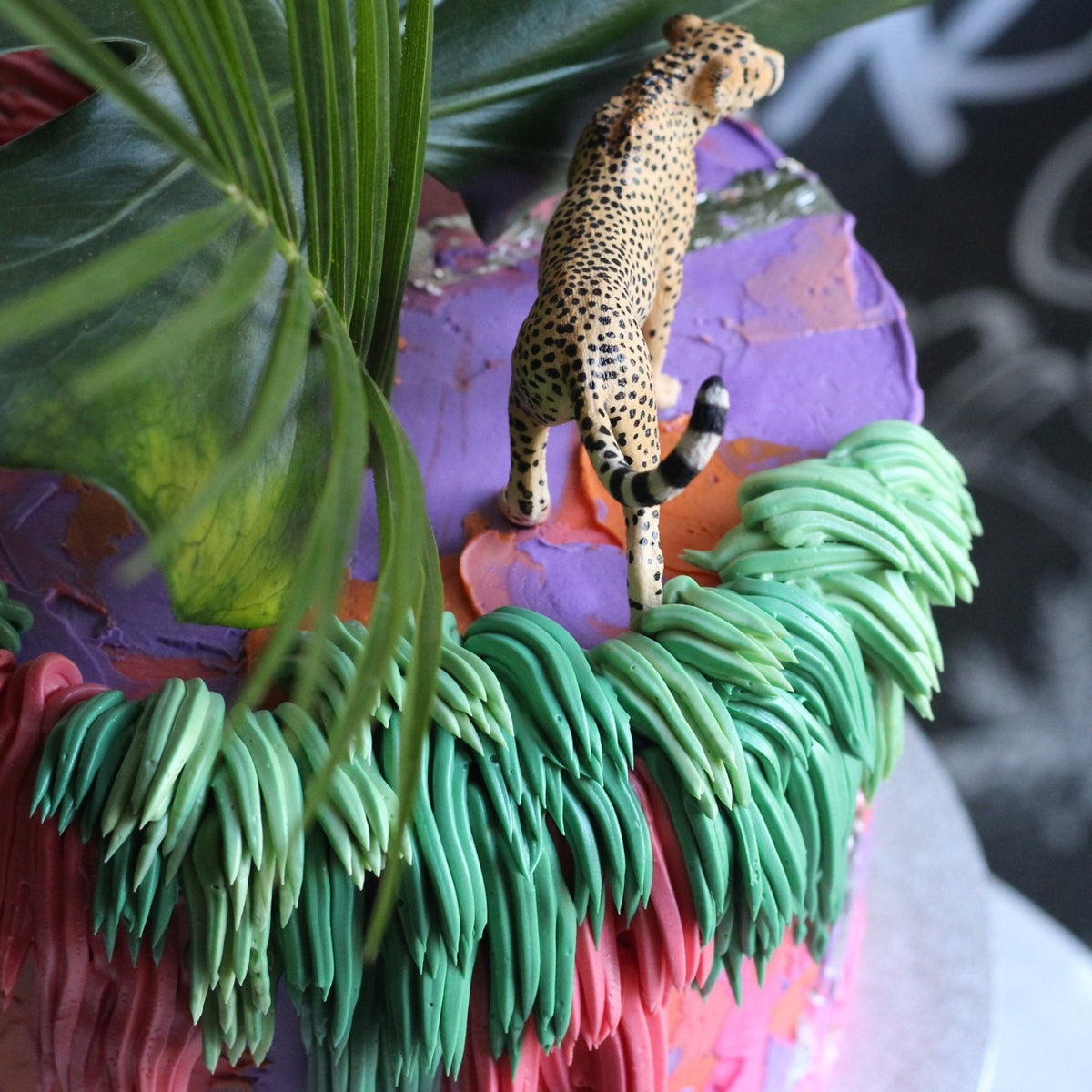 Utopia Cake - Bold colored icing and shaggy cream adorned with green leaves and a cheetah topper.