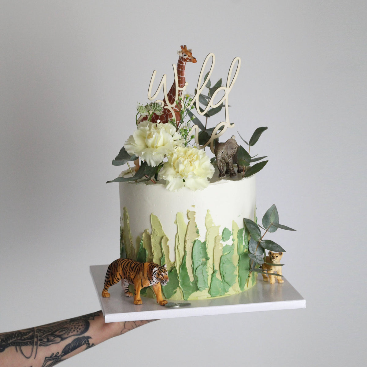 Der Safari Tour Cake – perfekt für alle, die weg wollen! Geschmückt mit Pinselstrichen, Blättern und einer Figur.