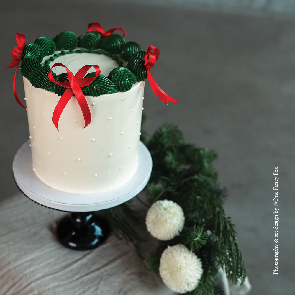 Chic white buttercream cake with green frills and festive red silk bows