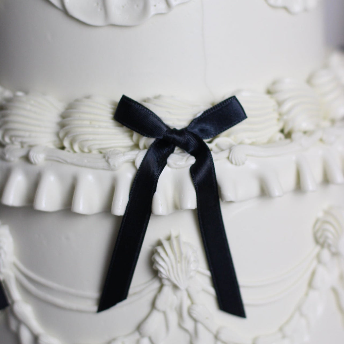Vintage-style white buttercream cake with elegant piping and black silk bows for a timeless finish.
