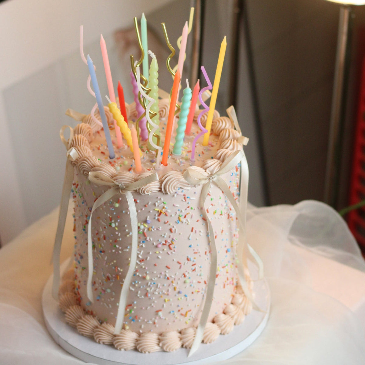 Customizable buttercream birthday cake with vintage piping, rainbow sprinkles, and ribbon bow details. Choose your preferred cake color and frill color, with an optional pastel candle add-on for an extra festive touch. Perfect for birthdays, celebrations, and special occasions in Berlin.