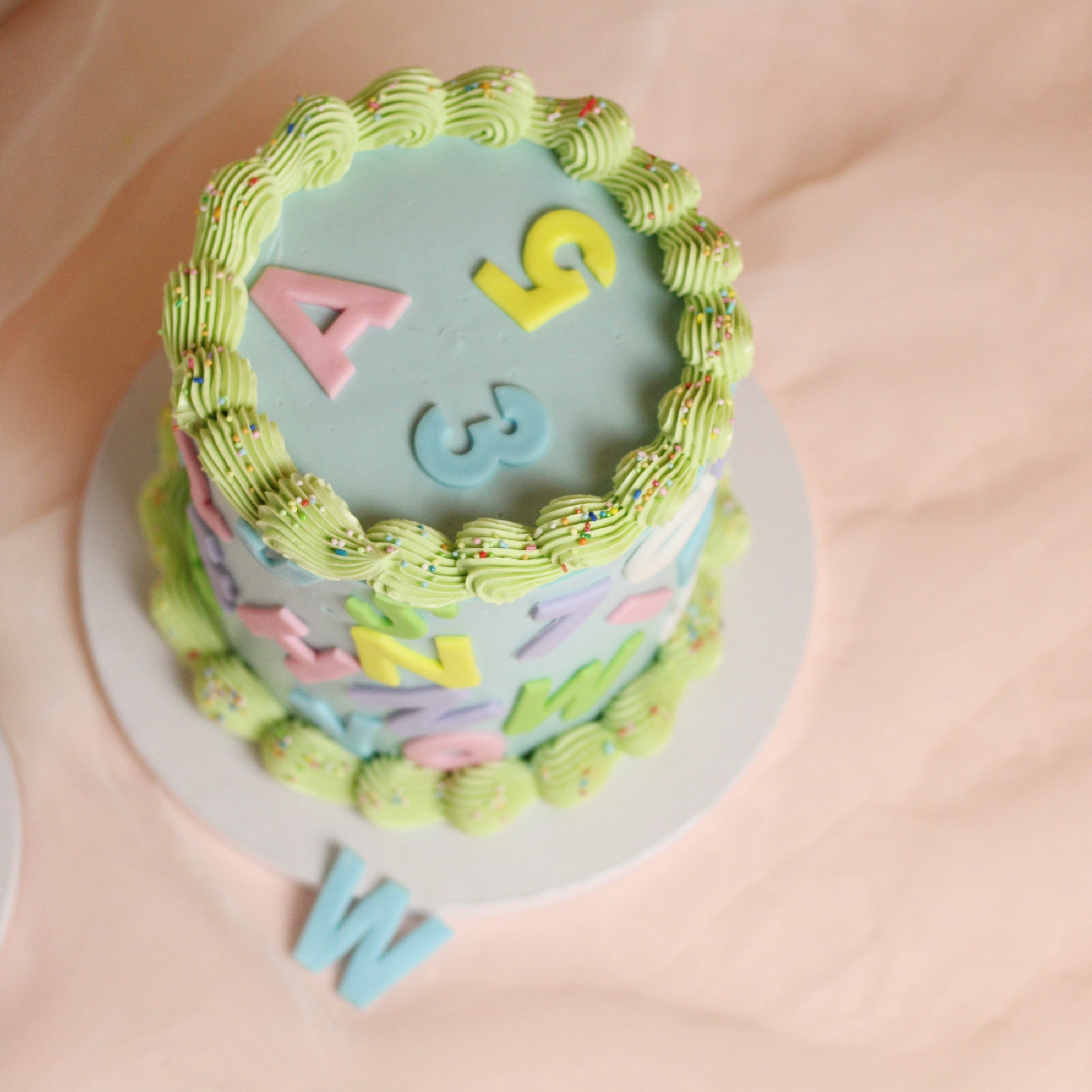 Celebrate the first day of school with our custom Einschulung Party cake. Features a smooth pastel buttercream base with colorful fondant letters, vintage piping, and a default dusting of sprinkles. The perfect centerpiece for a school enrollment party!