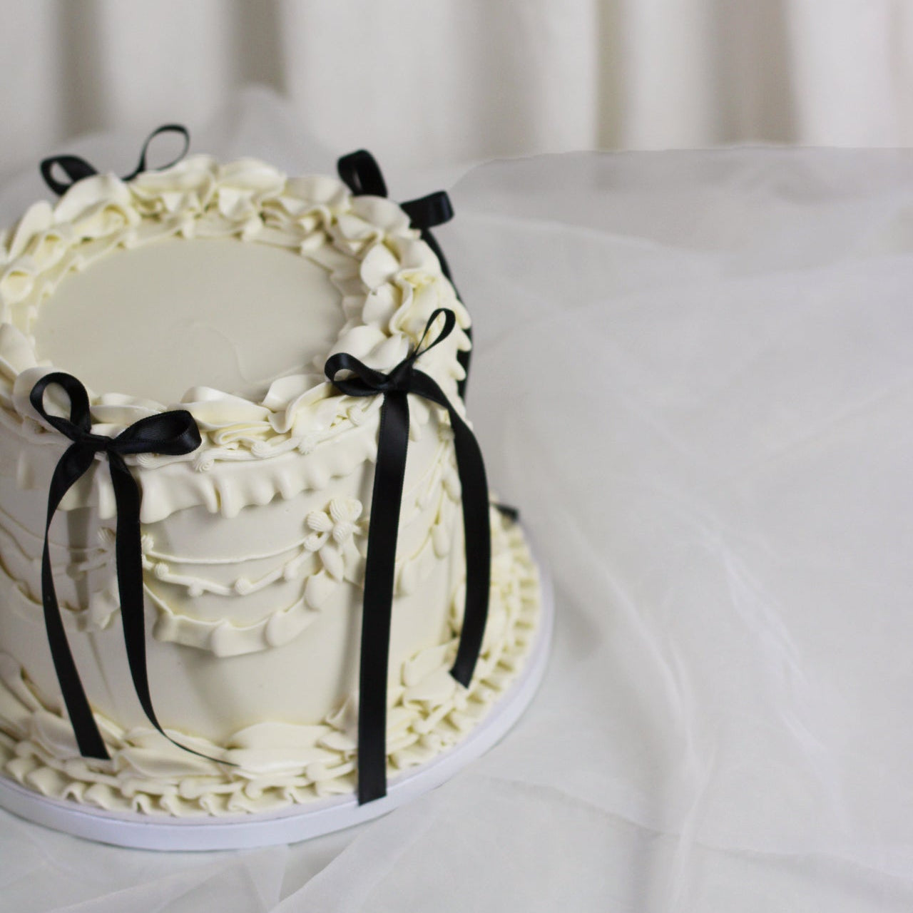 Vintage-style white buttercream cake with elegant piping and black silk bows for a timeless finish.

