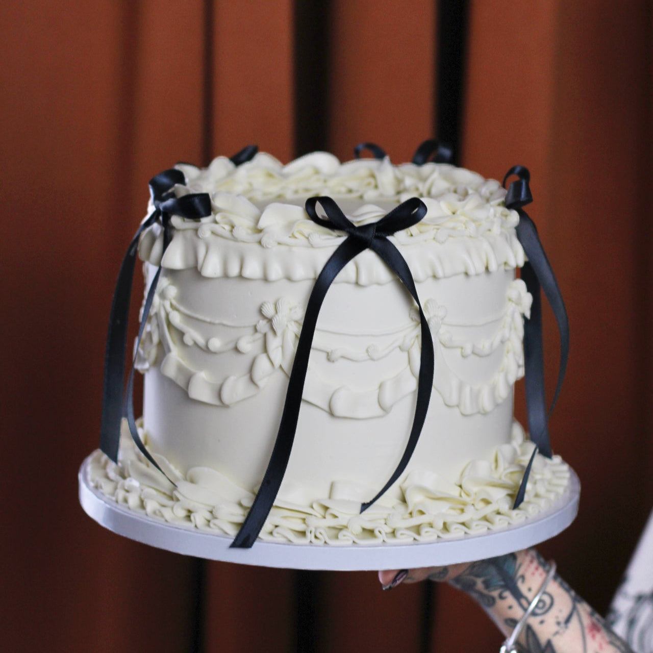Vintage-style white buttercream cake with elegant piping and black silk bows for a timeless finish.
