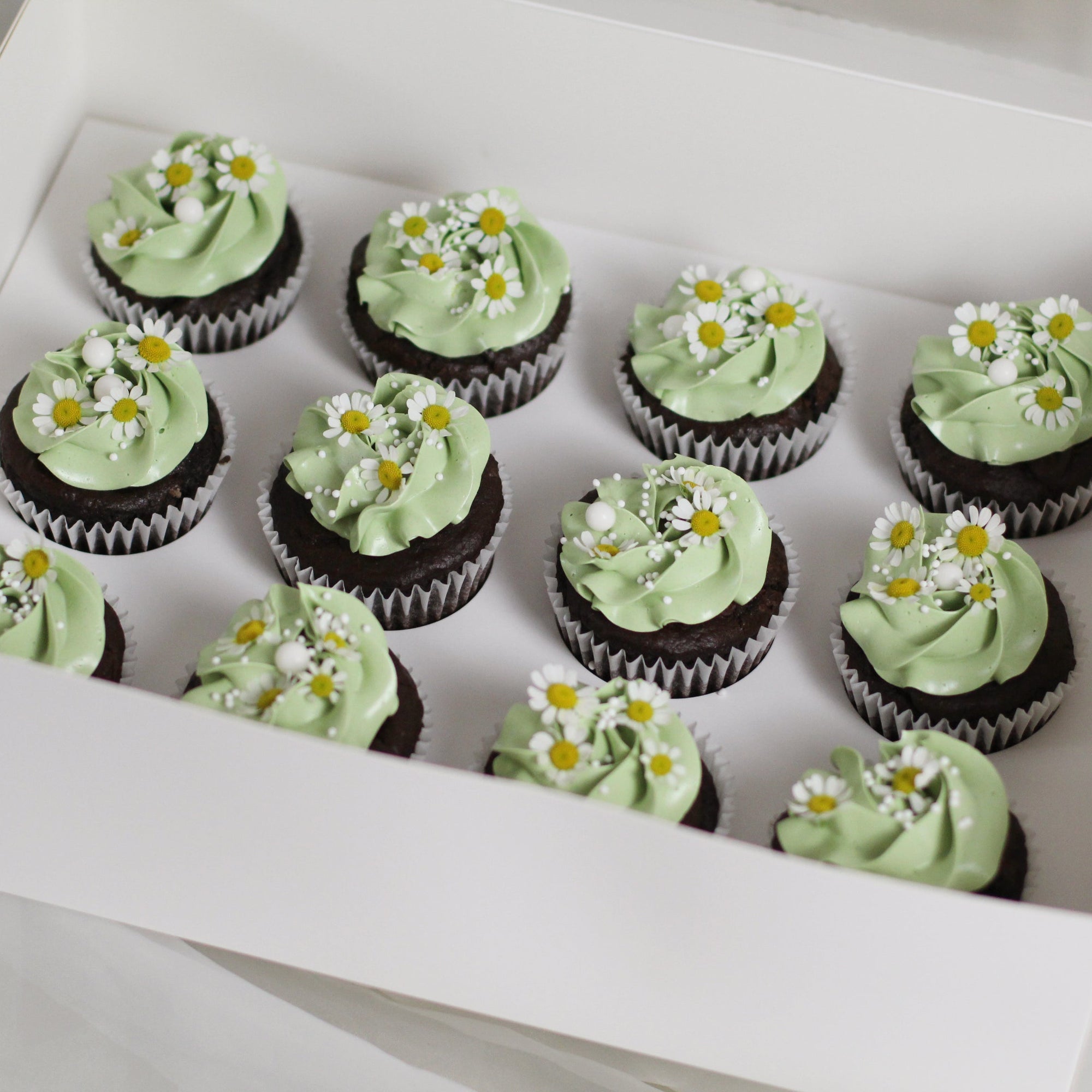 Our signature cupcakes with pastel green buttercream, adorned with daisies on top.