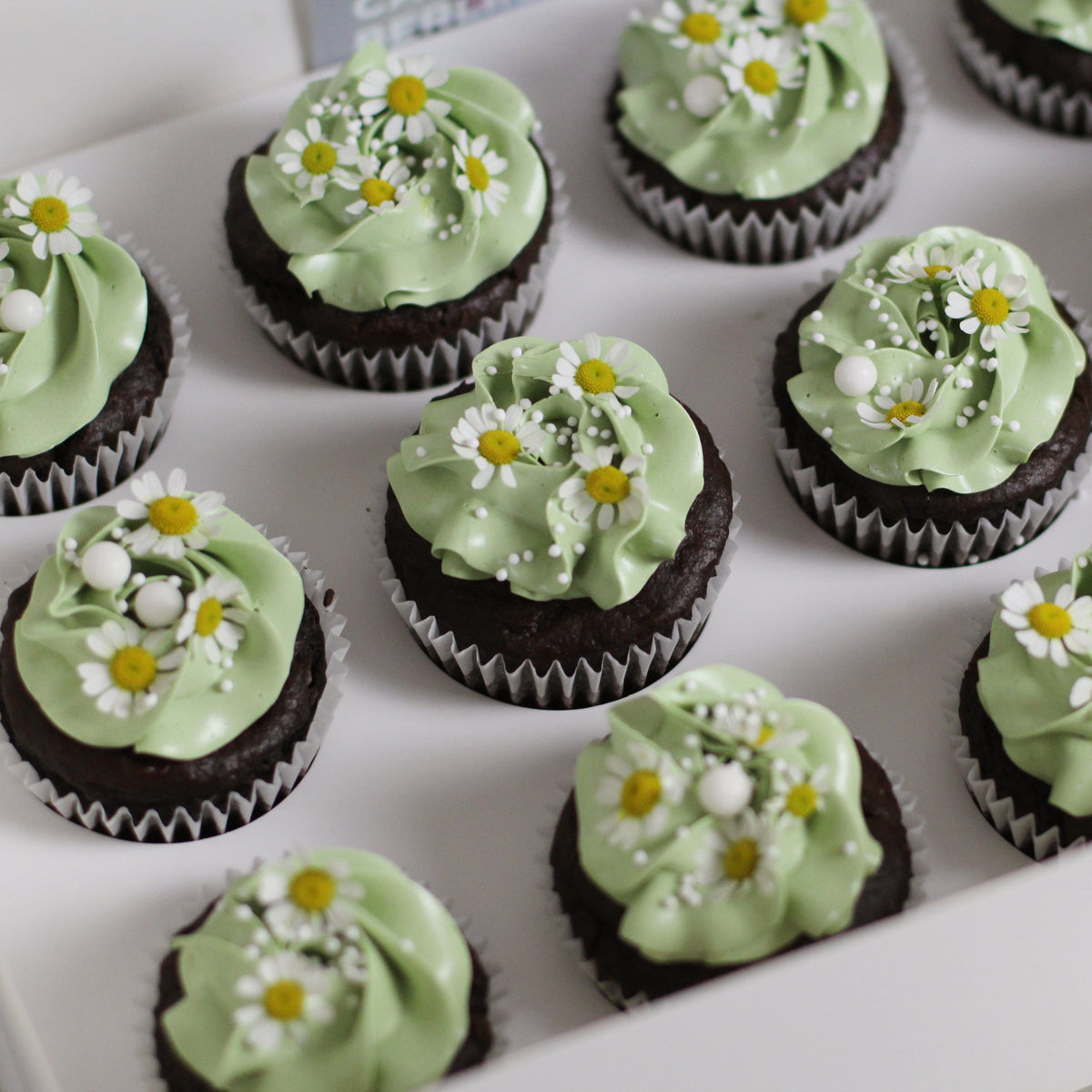 Our signature cupcakes with pastel green buttercream, adorned with daisies on top.