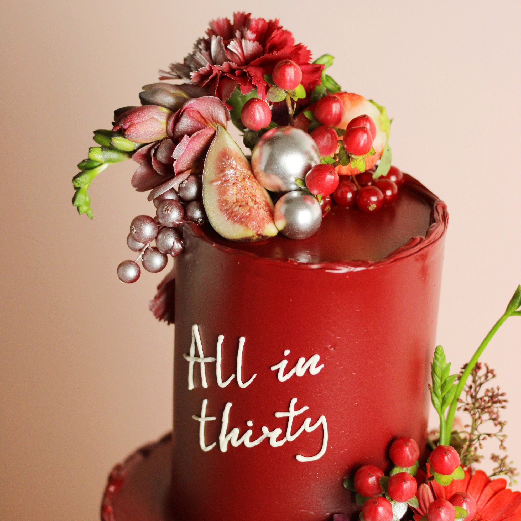 Wine-red celebration cake with figs, berries, and fresh florals. Elegant two-tier design for birthdays and special events.