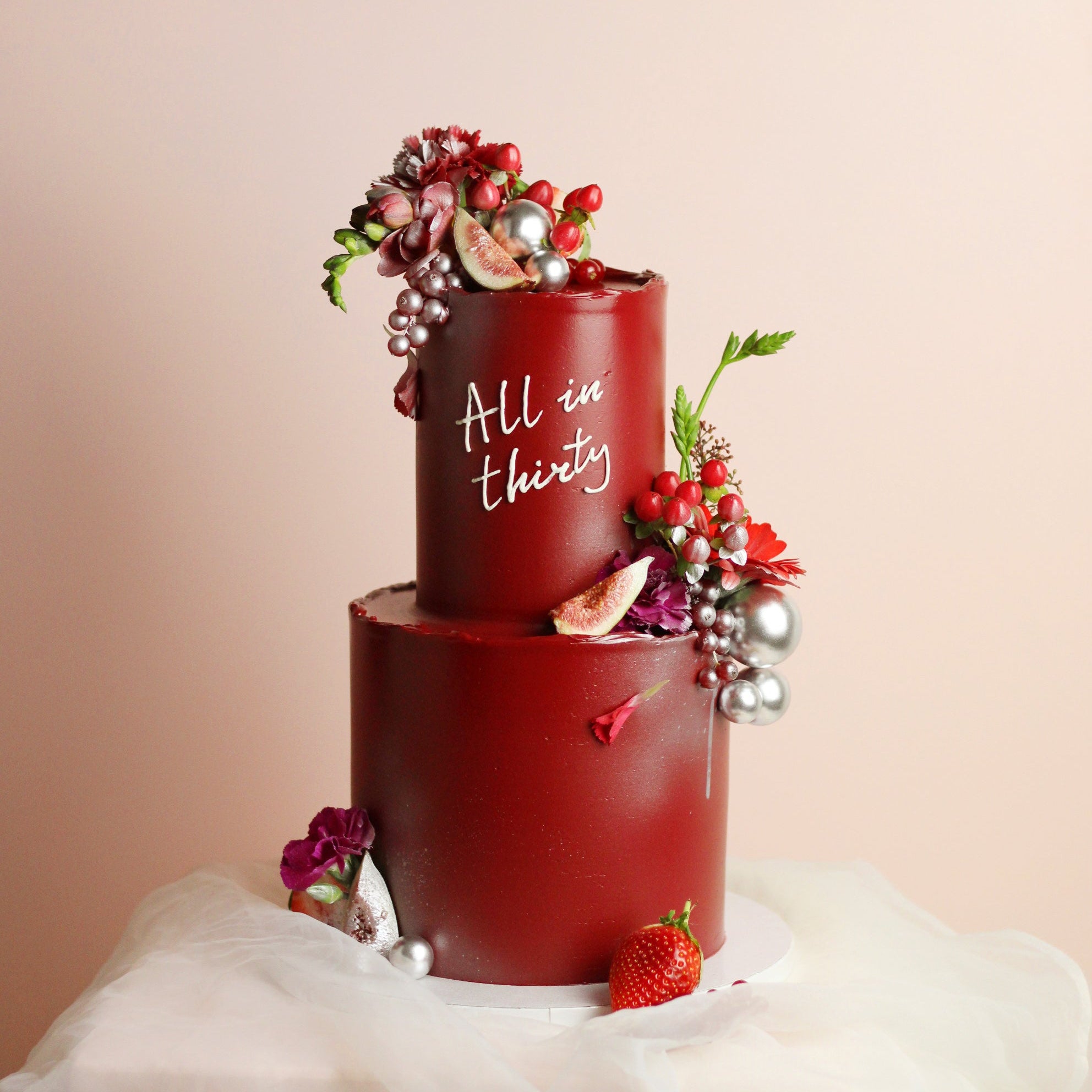 Wine-red celebration cake with figs, berries, and fresh florals. Elegant two-tier design for birthdays and special events.