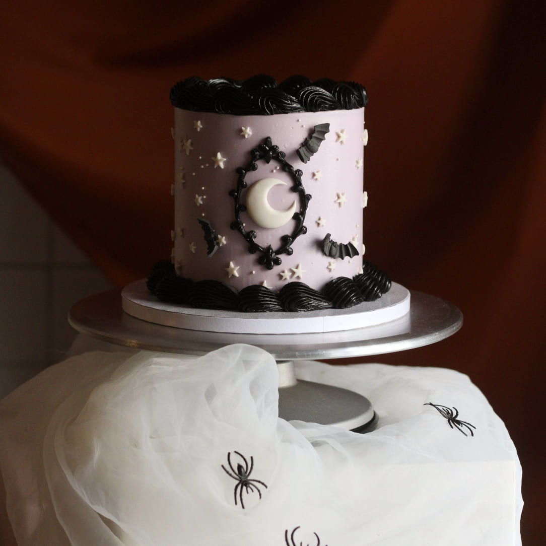 A delicious, creepy vintage cake decorated with night sky details on a spiderweb stand. Join our halloween cake decorating workshop in Berlin and learn to make that instagrammable cake yourself. A super fun activity for friends! Tolles To-Do in Berlin für alle Cake Lovers. Perfekt für deine nächste Halloween Party!