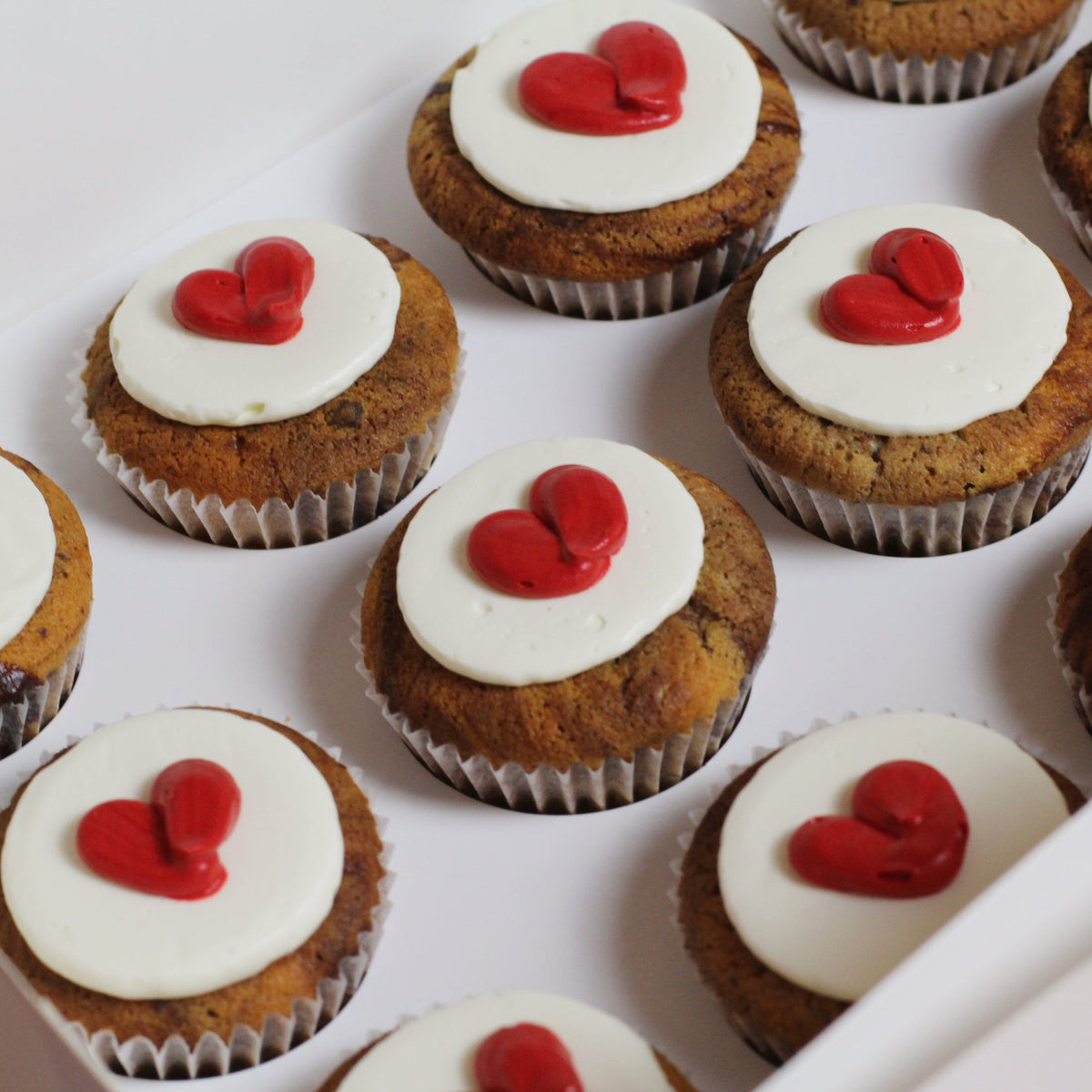 QUEEN OF HEARTS Cupcakes decorated with white fluffy icing and fiery red hearts on top.
