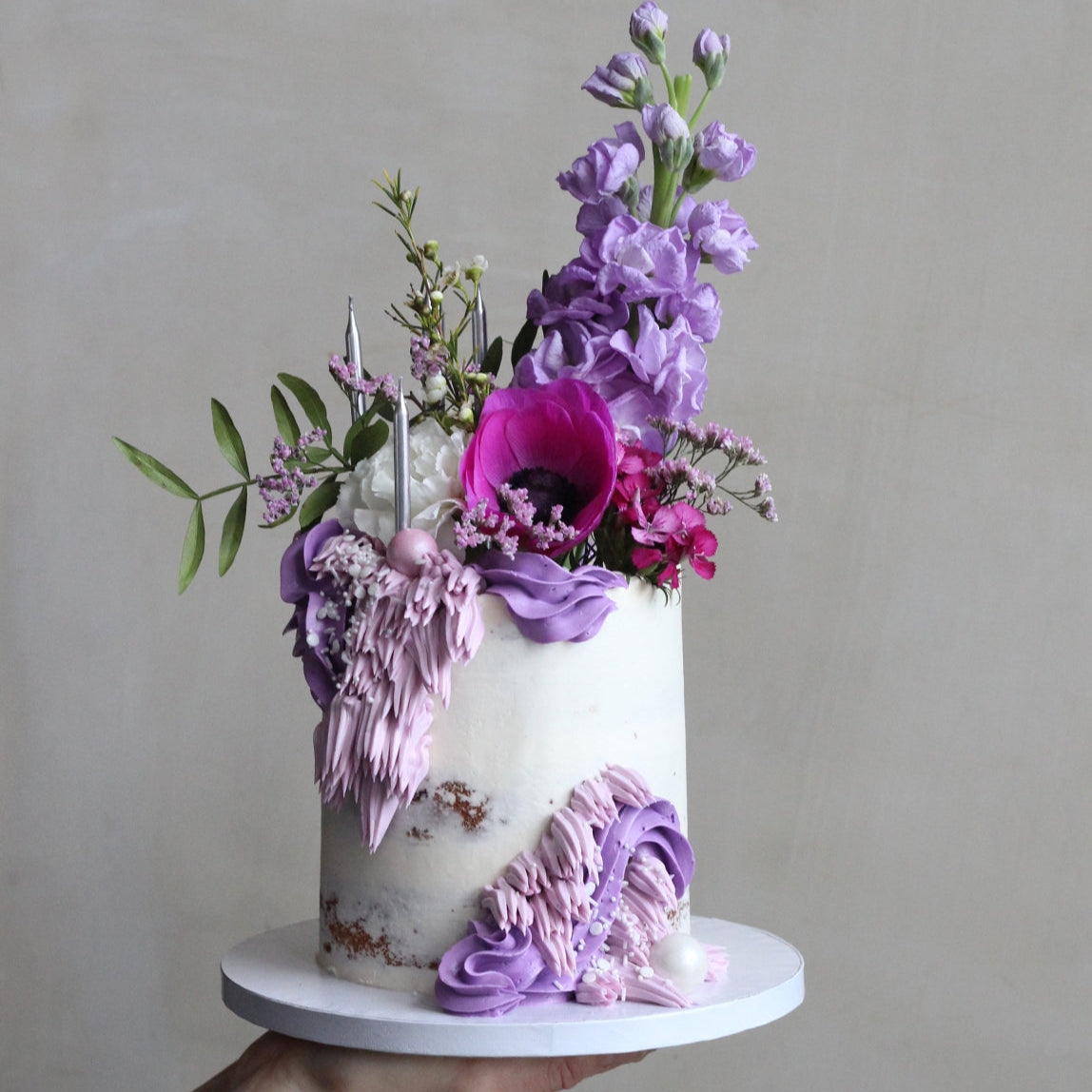 Semi naked cake, dfeocrated with seasonal fresh flowers in purple andpink shaeds and a touch of buttercream frills.