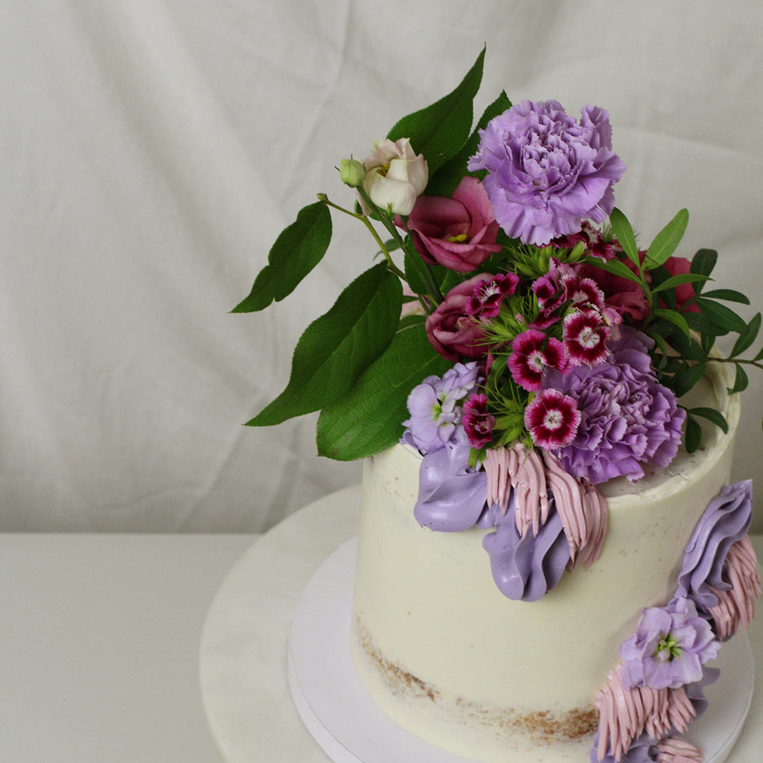 Semi-naked cake adorned with purple florals and greens