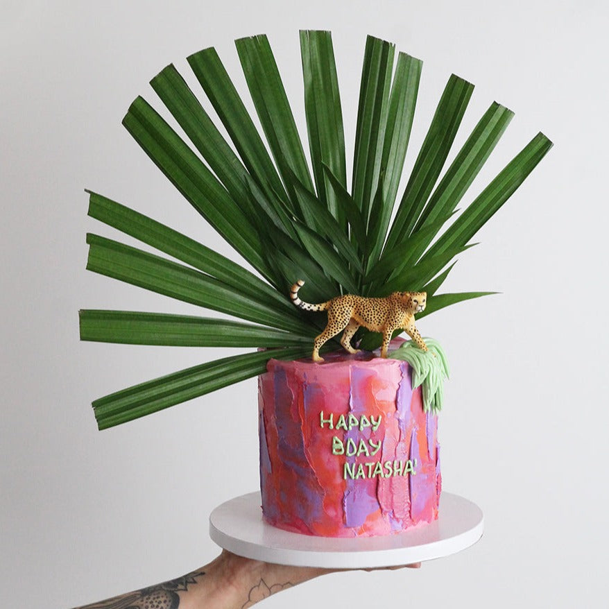 Utopia Cake - Bold colored icing and shaggy cream adorned with green leaves and a cheetah topper. 