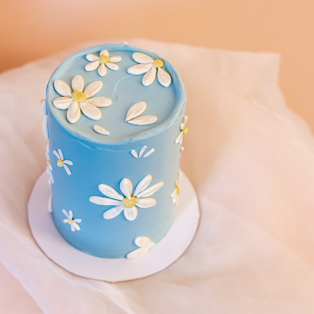Elegant Easter cake with a soft blue buttercream base and hand-piped white daisies, created in collaboration with Sawade. A modern, floral centerpiece for spring celebrations.