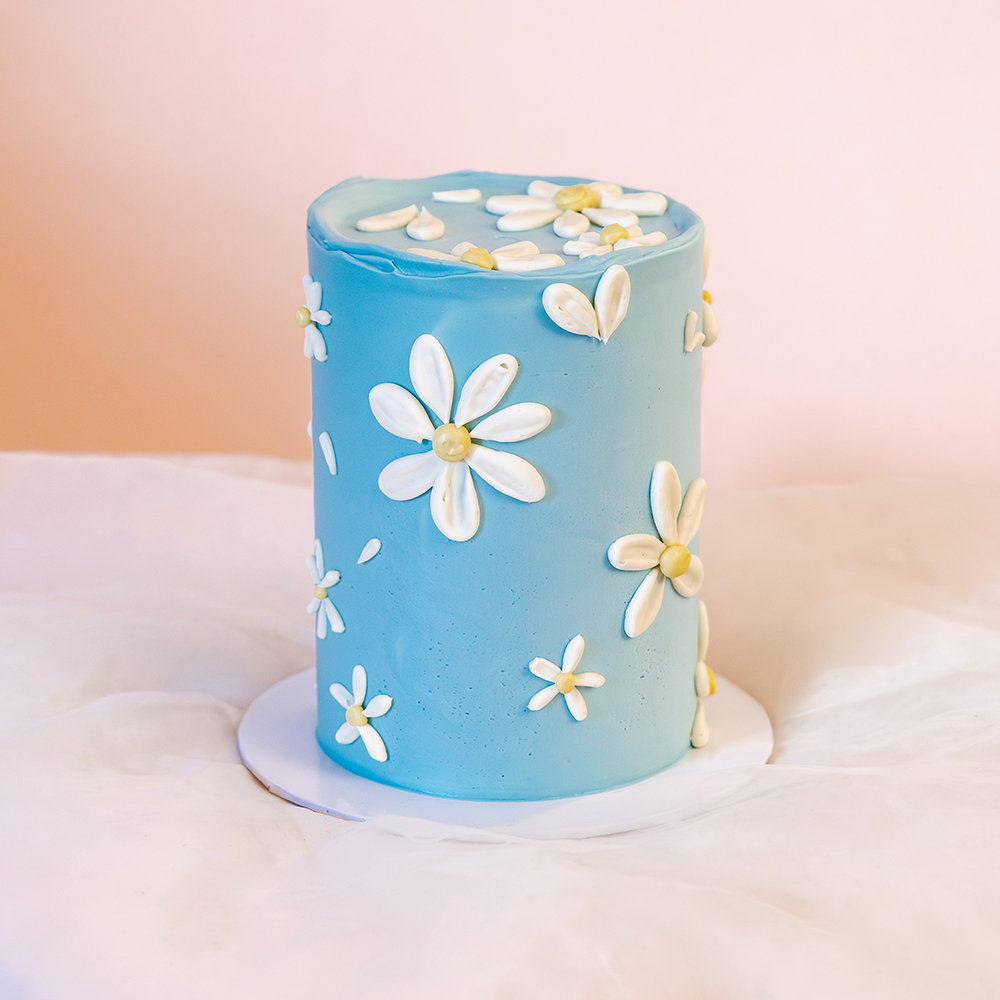 Elegant Easter cake with a soft blue buttercream base and hand-piped white daisies, created in collaboration with Sawade. A modern, floral centerpiece for spring celebrations.