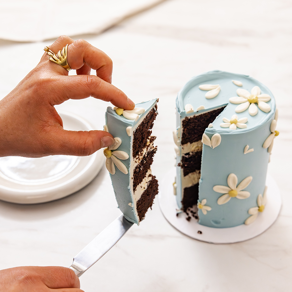 Elegant Easter cake with a soft blue buttercream base and hand-piped white daisies, created in collaboration with Sawade. A modern, floral centerpiece for spring celebrations.