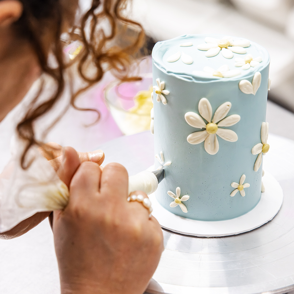 Elegant Easter cake with a soft blue buttercream base and hand-piped white daisies, created in collaboration with Sawade. A modern, floral centerpiece for spring celebrations.