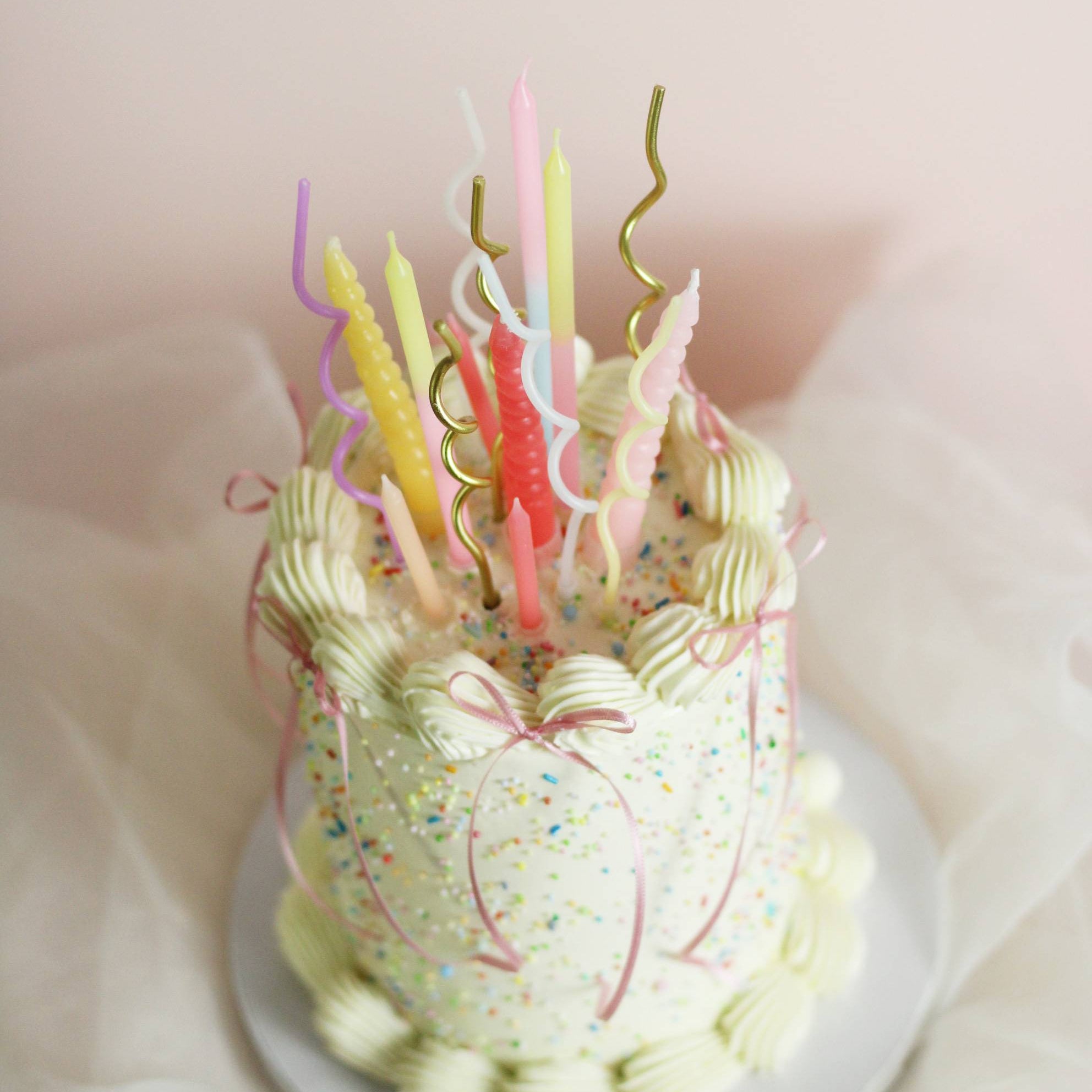 Customizable buttercream birthday cake with vintage piping, rainbow sprinkles, and ribbon bow details. Choose your preferred cake color and frill color, with an optional pastel candle add-on for an extra festive touch. Perfect for birthdays, celebrations, and special occasions in Berlin.