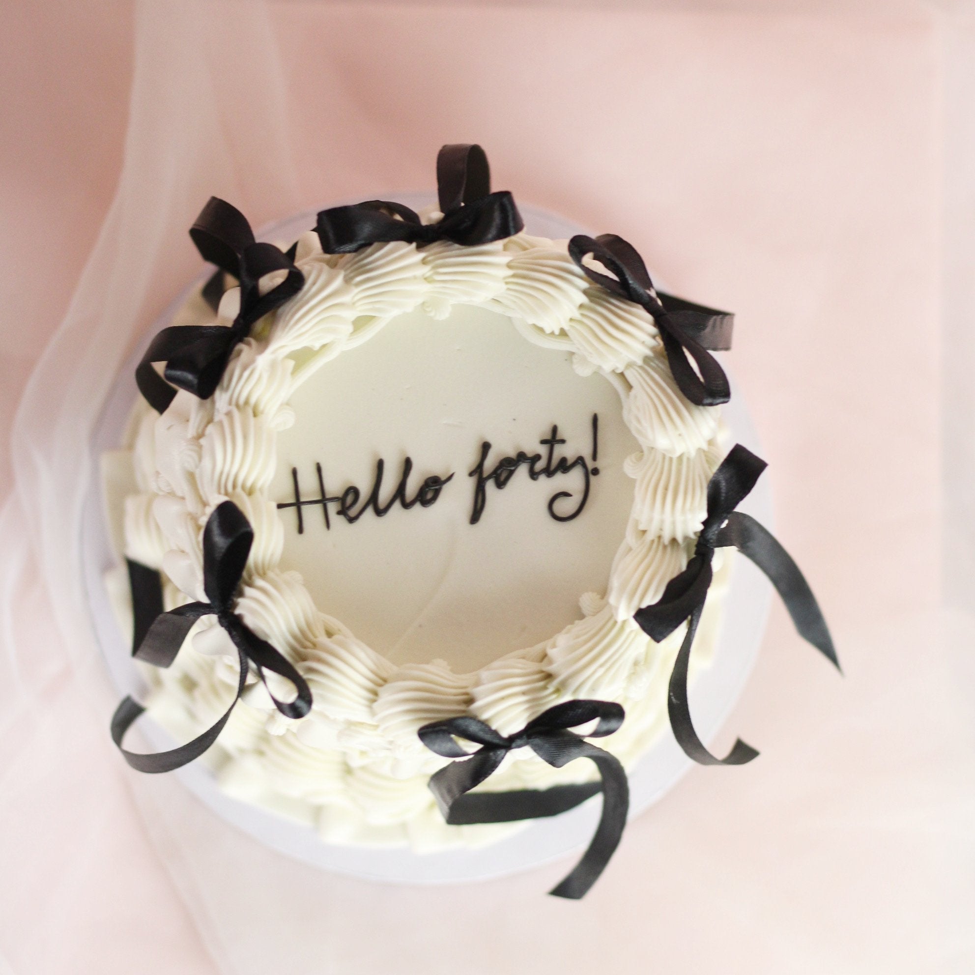 Vintage-style white buttercream cake with elegant piping and black silk bows for a timeless finish.
