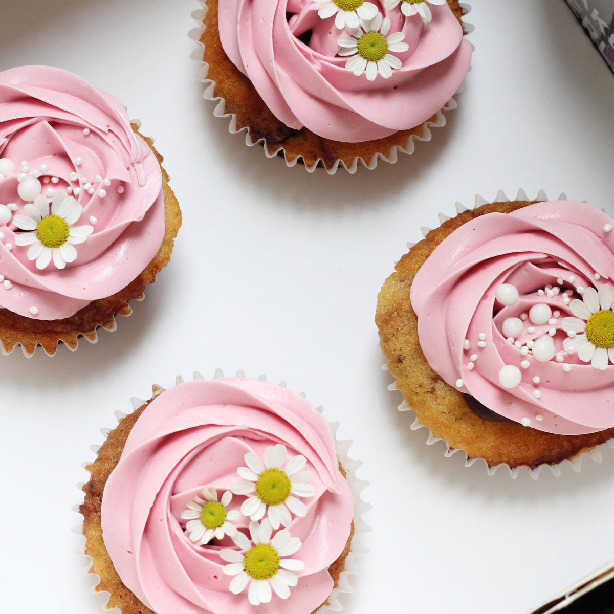 Our signature cupcakes with pink buttercream, adorned with daisies on top!