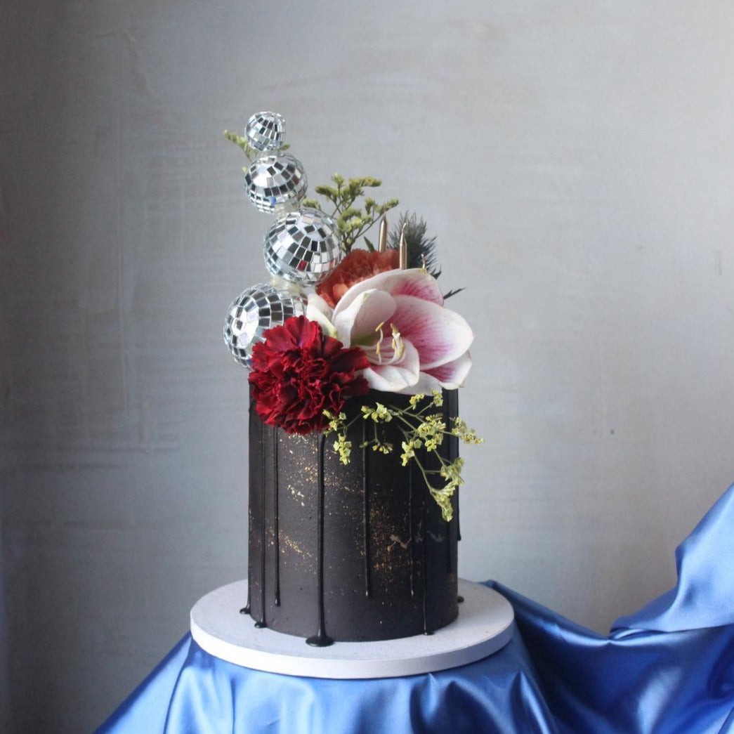 Discovery Cake - a striking black-iced creation topped with bold flowers and sparkling disco balls. The perfect statement cake for parties, birthdays, and celebrations.