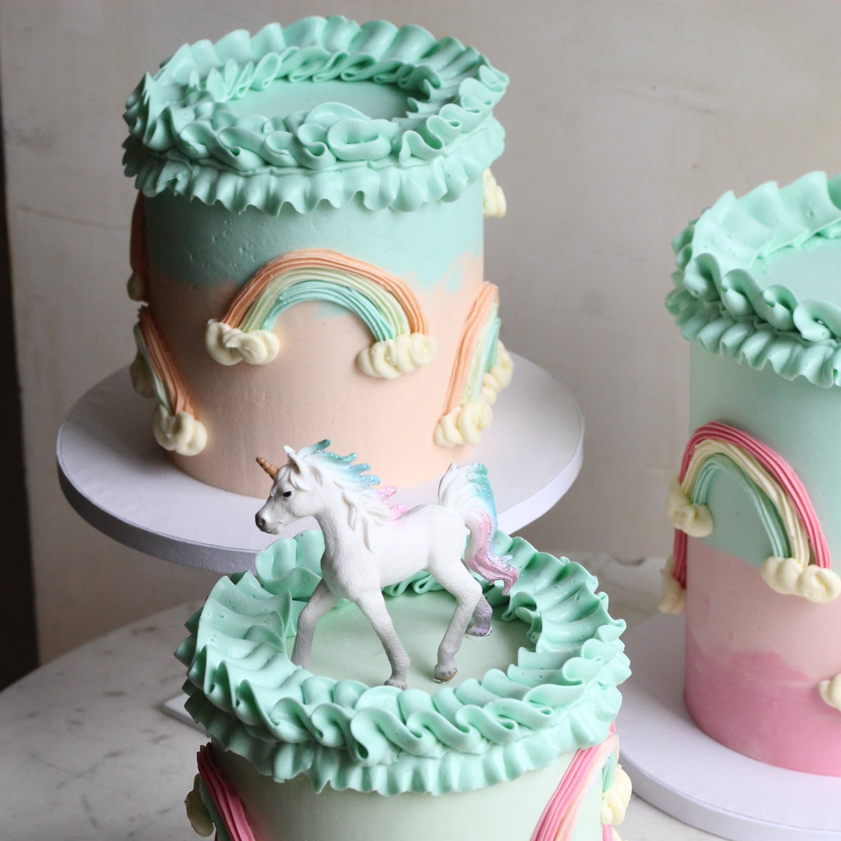 Our Rainbow Cake with peach &amp; mint ombre icing, 3D rainbows, creamy ruffles and unicorn topper!