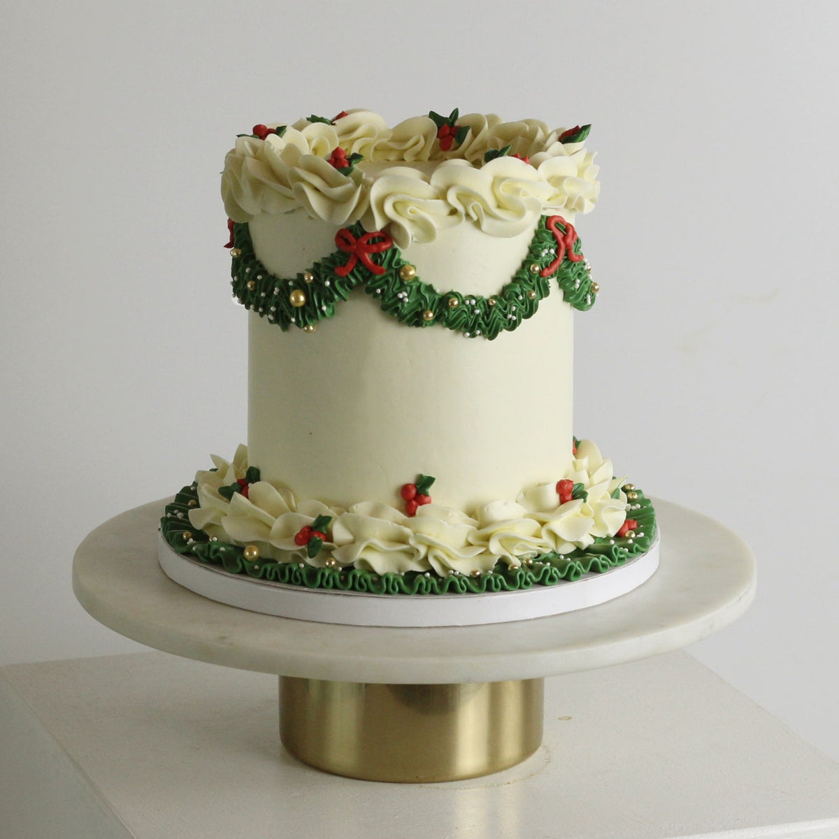 Elegant white Christmas cake with green buttercream and red bows, gold details, perfect for festive holiday celebrations and seasonal dessert tables.