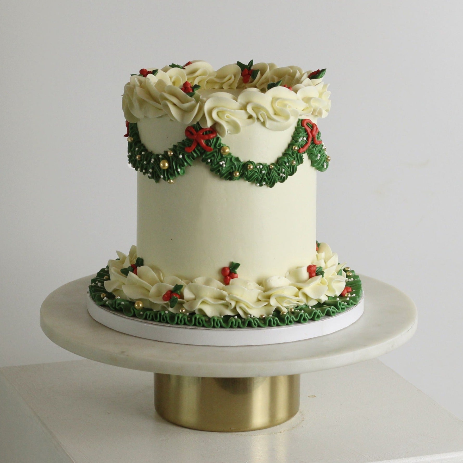 Elegant white Christmas cake with green buttercream and red bows, gold details, perfect for festive holiday celebrations and seasonal dessert tables.