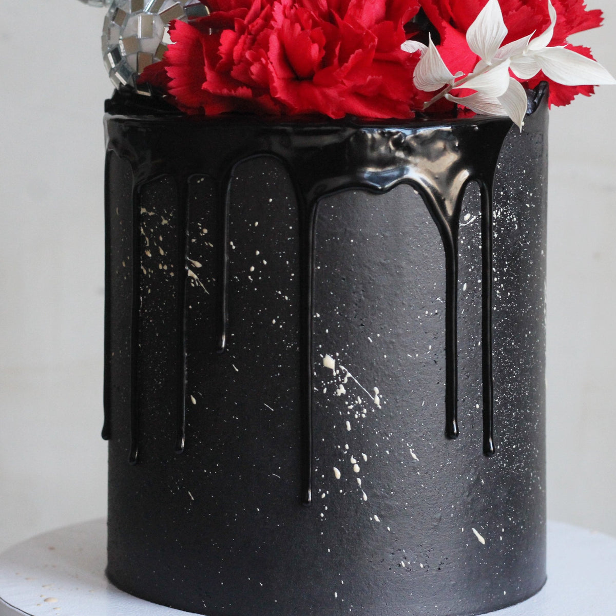 A true statement cake featuring sleek black-on-black icing, a dazzling disco ball headpiece, and bold floral details. Perfect for glamorous parties and unforgettable celebrations.