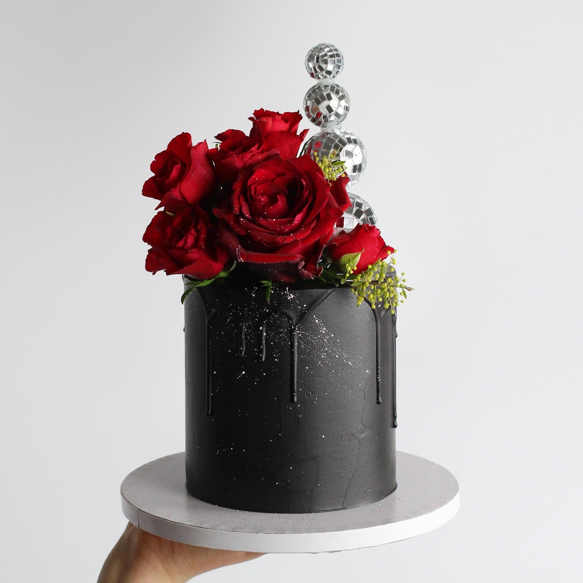 A true statement cake featuring sleek black-on-black icing, a dazzling disco ball headpiece, and bold floral details. Perfect for glamorous parties and unforgettable celebrations.