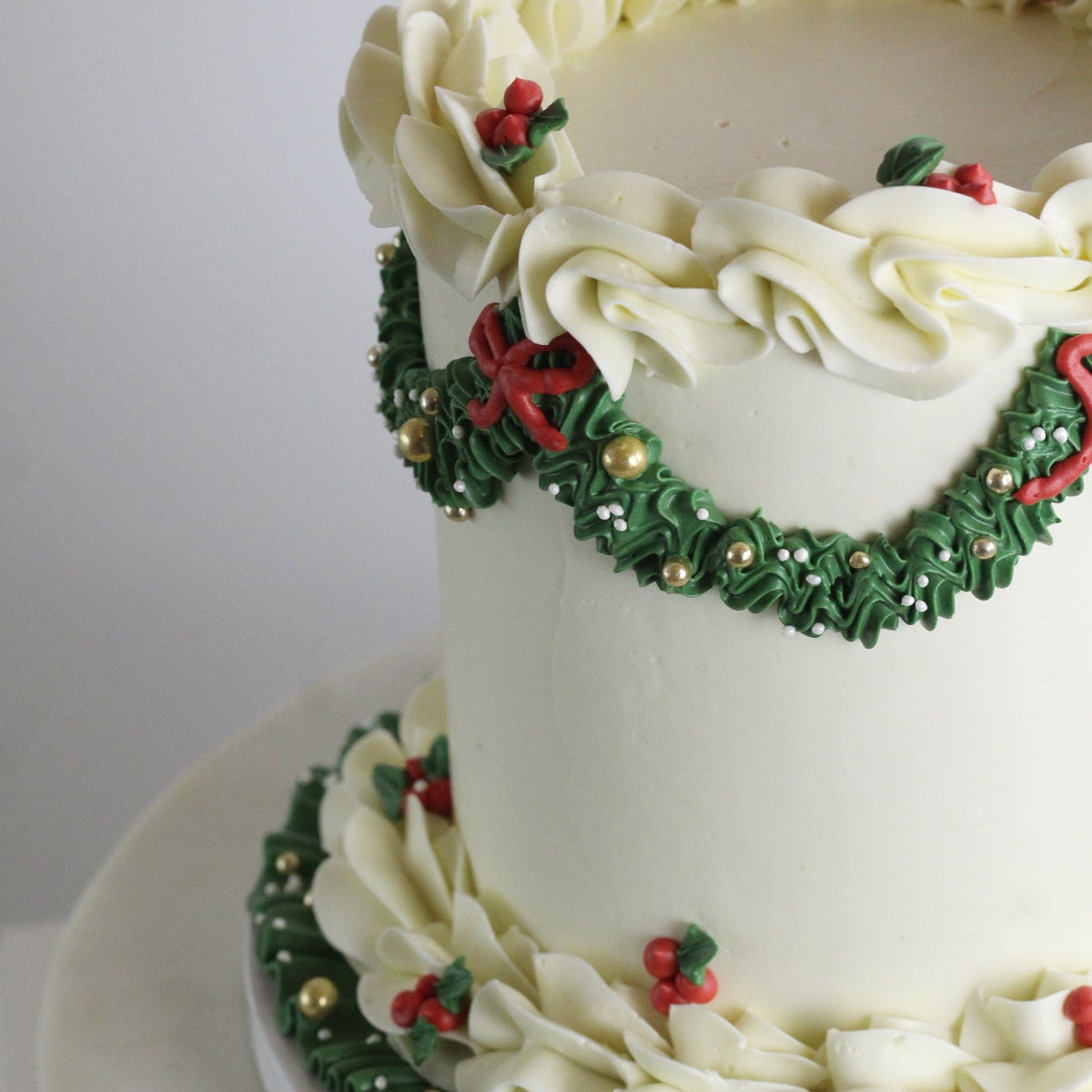 Elegant white Christmas cake with green buttercream and red bows, gold details, perfect for festive holiday celebrations and seasonal dessert tables.