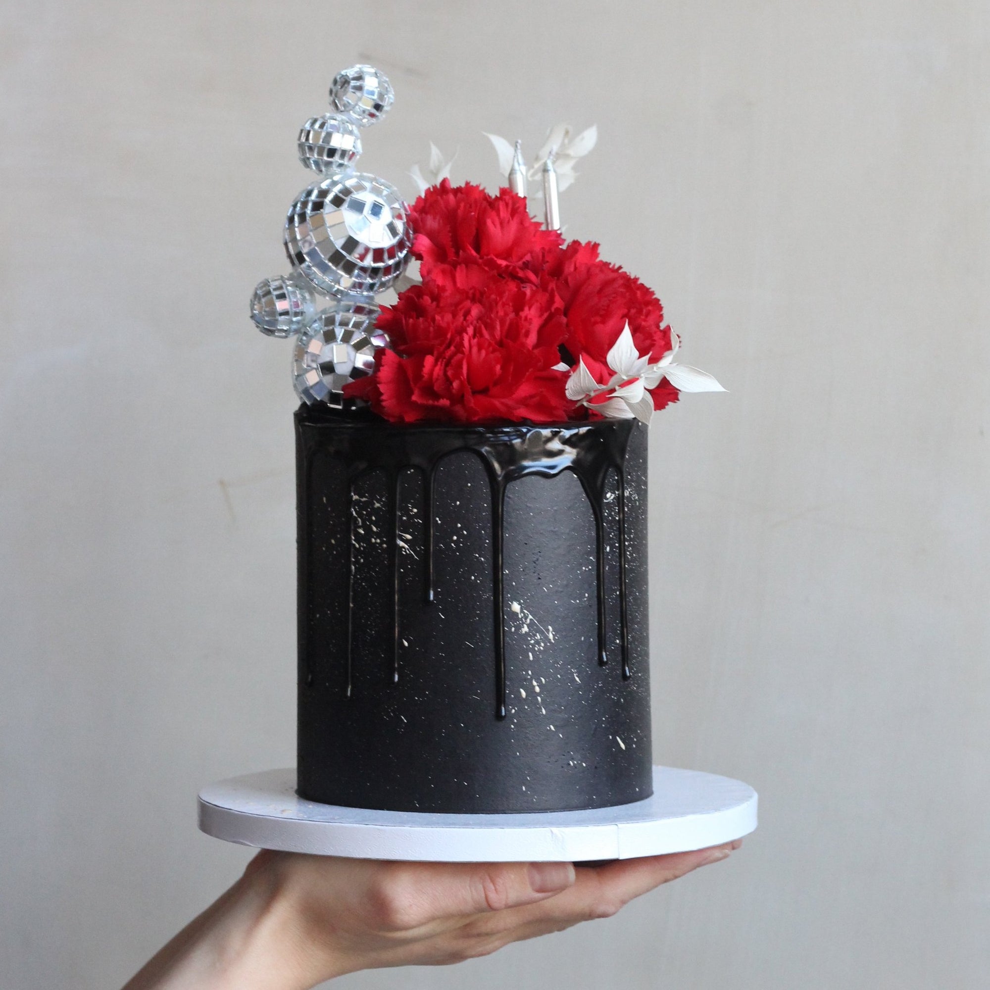 A true statement cake featuring sleek black-on-black icing, a dazzling disco ball headpiece, and bold floral details. Perfect for glamorous parties and unforgettable celebrations.